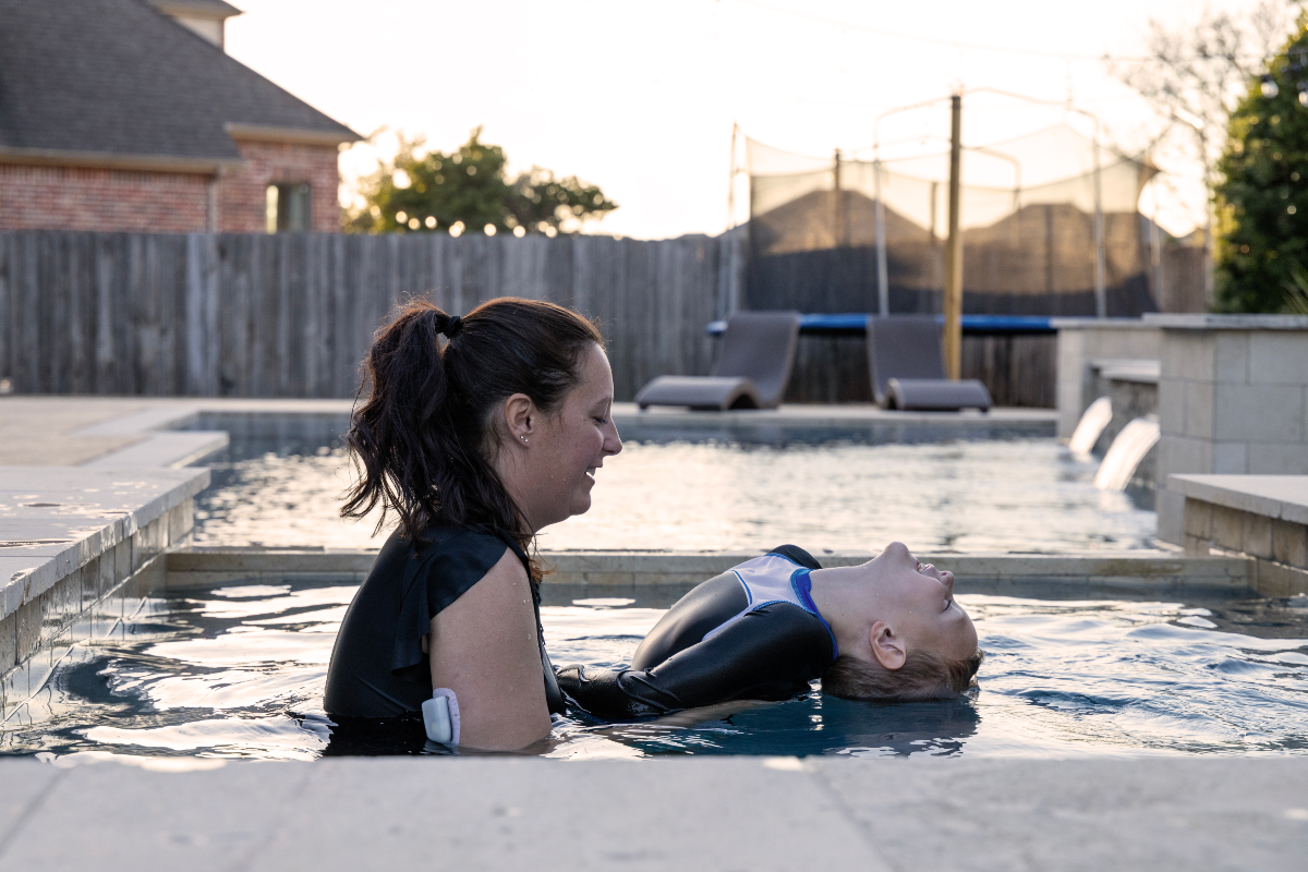 Omnipod Podder in a pool with pod on her right arm while holding up a boy